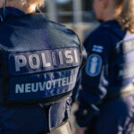 Lähikuva kahdesta poliisista. Toisen selässä tummansinisessä liivissä lukee valkoisilla kirjaimilla "POLIISI" ja "NEUVOTTELIJA". Toisen poliisin hihassa näkyy Suomen lippu ja poliisin miekkaleijonatunnus.