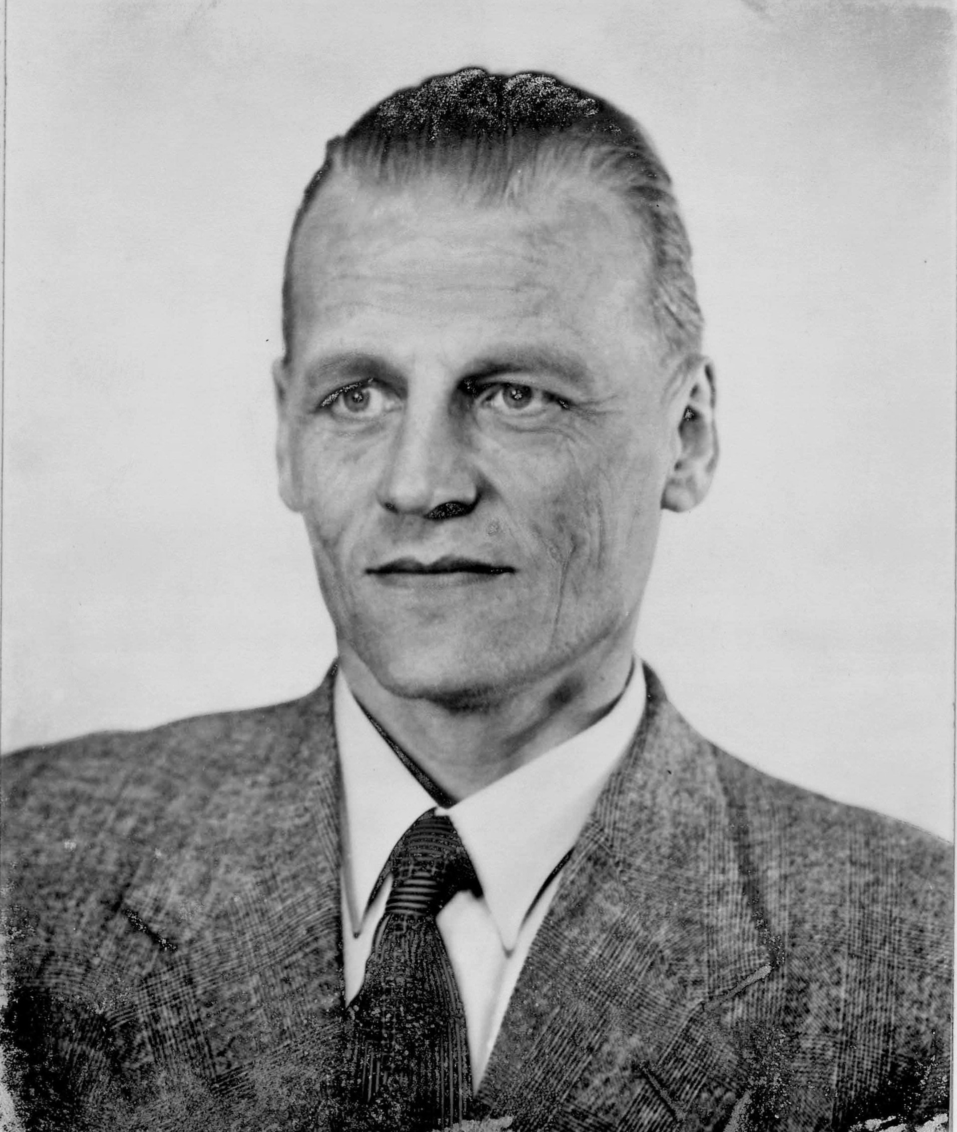 Mustavalkoinen kasvokuva miehestä,njolla on puku, valkoinen paita ja kravatti sekä lyhyet hiukset.